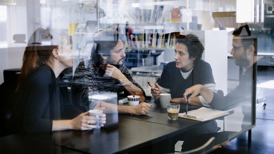 Gruppbild på personal vid Arktiekthögskolan som sitter och pratar och dricker kaffe vid ett bord.