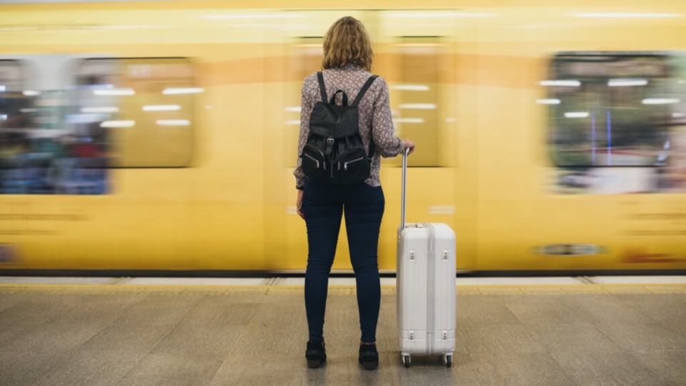 Woman on a train platform with a yellow train speeding past.