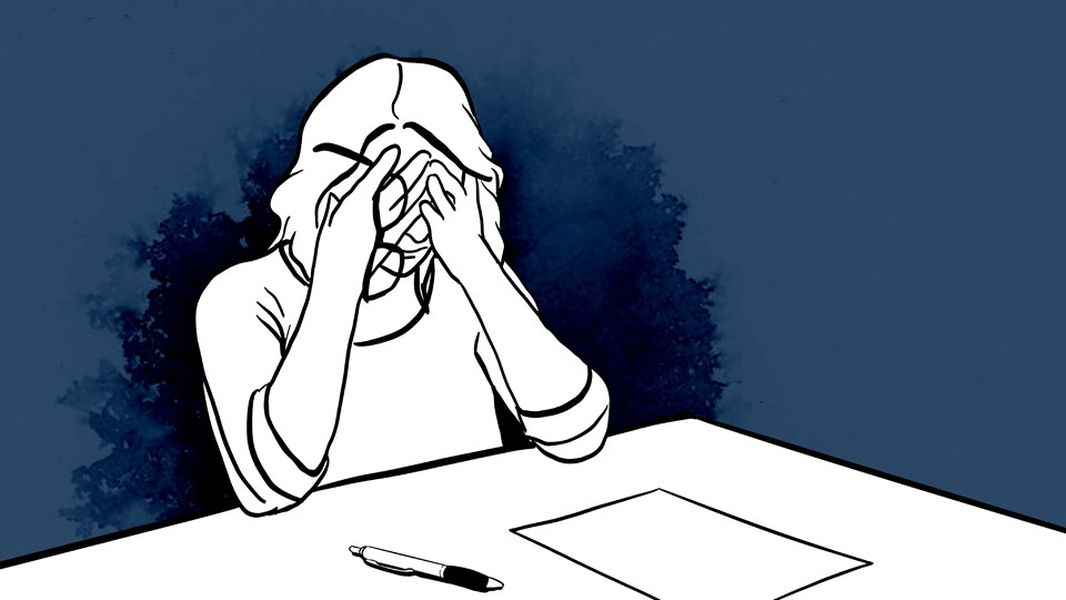 En person vid skrivbordet med penna och papper. Personen har händerna för ansiktet och ser ängslig ut.